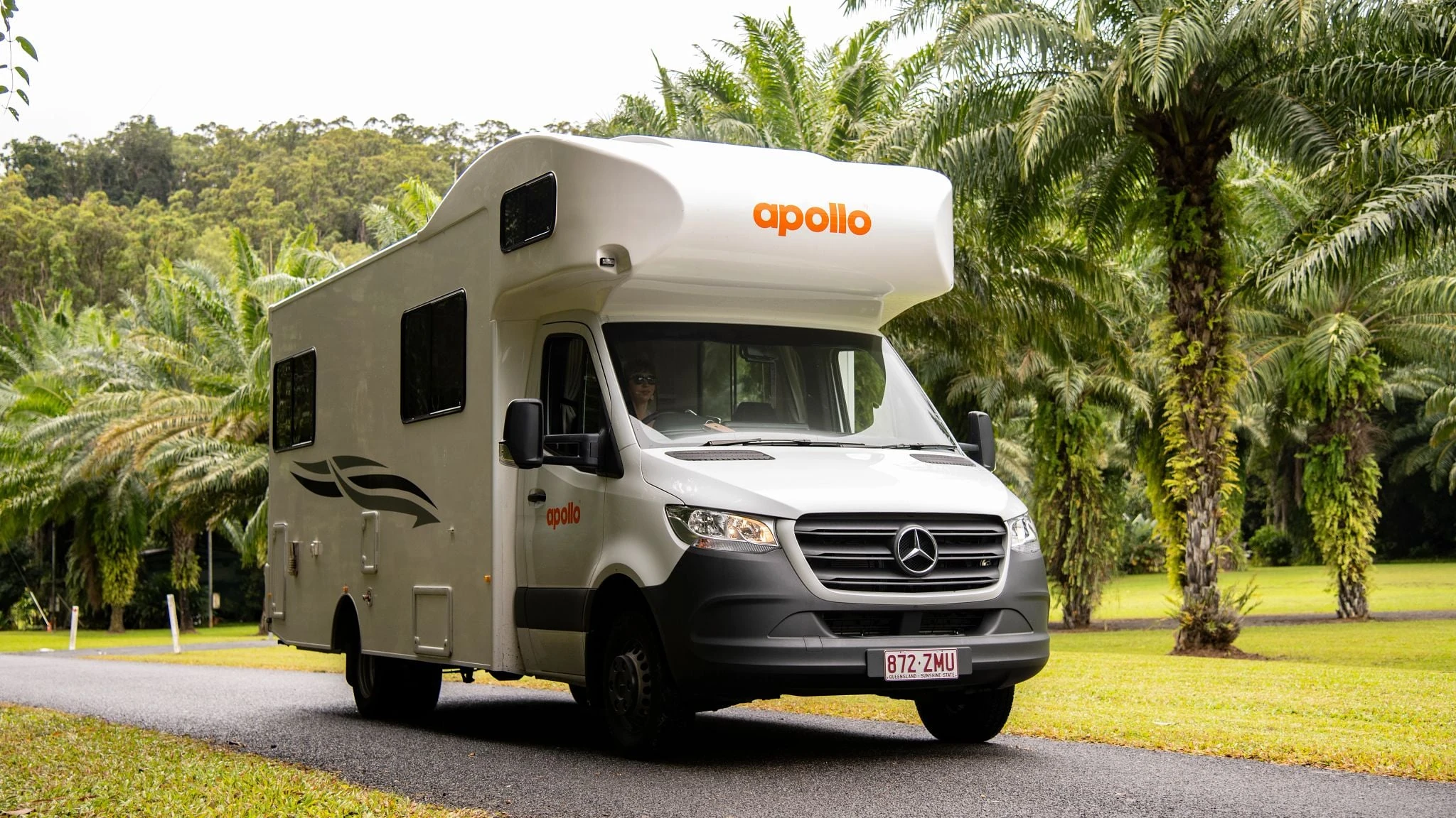 Apollo Euro motorhome with prominent orange branding driving through tropical Queensland, Australia